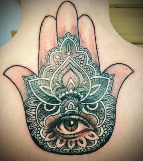 A realistic eye stares out from the palm of this religious hamsa hand tattoo decorated with mandala designs