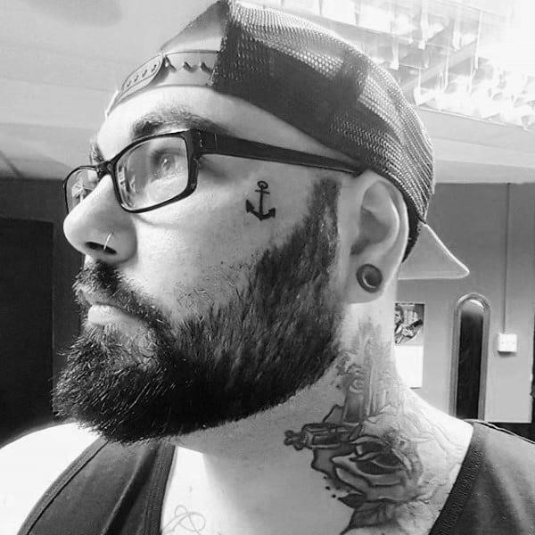 Small face tattoo of anchor on male